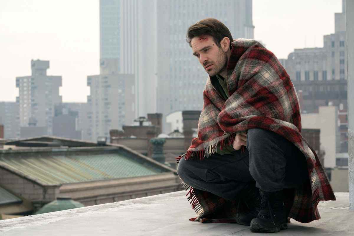 Charlie Cox dans le rôle de Matt Murdock enveloppé dans une couverture sur un toit avec une entaille sur la tête en pensant à la vie avec New York en arrière-plan