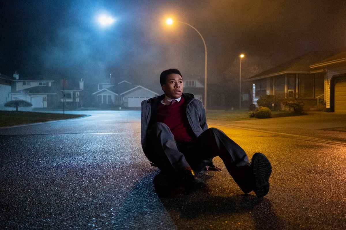 Un personnage de Midnight Club assis par terre, très surpris par quelque chose hors caméra ;  il est assis dans la rue d'un cul de sac de banlieue 