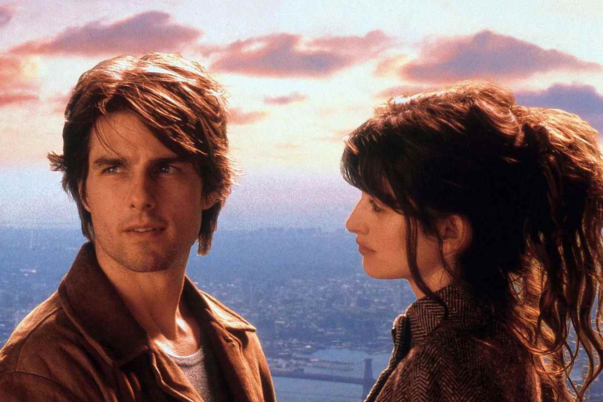 Un homme (Tom Cruise) détourne le regard d'une femme (Penélope Cruz) alors qu'il se tient devant un coucher de soleil idyllique avec une ligne d'horizon de New York au loin.