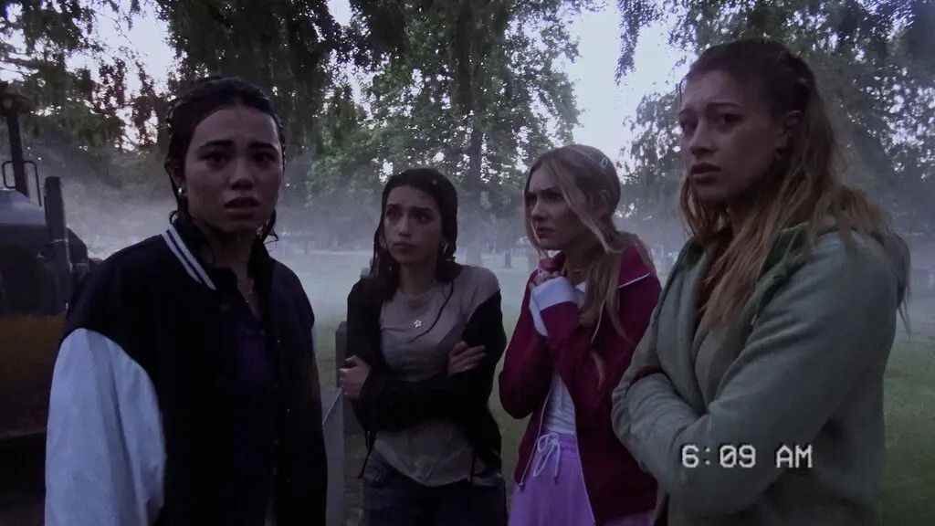 Quatre jeunes femmes se tiennent l'une à côté de l'autre, regardant fixement une caméra vidéo et semblant visiblement inquiètes alors qu'elles sont entourées d'arbres et de brouillard.