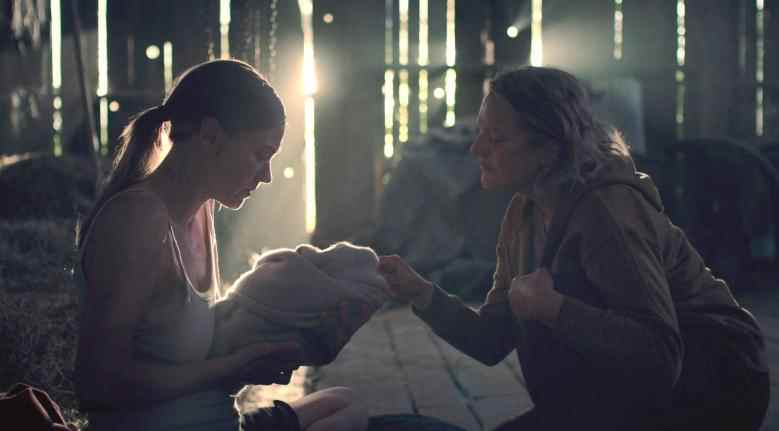 Deux femmes dans une grange, l'une d'elles berçant un nouveau-né emmitouflé dans des couvertures ;  encore de "Le conte de la servante."