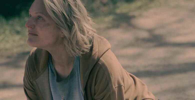 A blonde woman with bruises and cuts on her face, kneeling on a dirt road and looking up at someone O.S.; still from "The Handmaid's Tale"