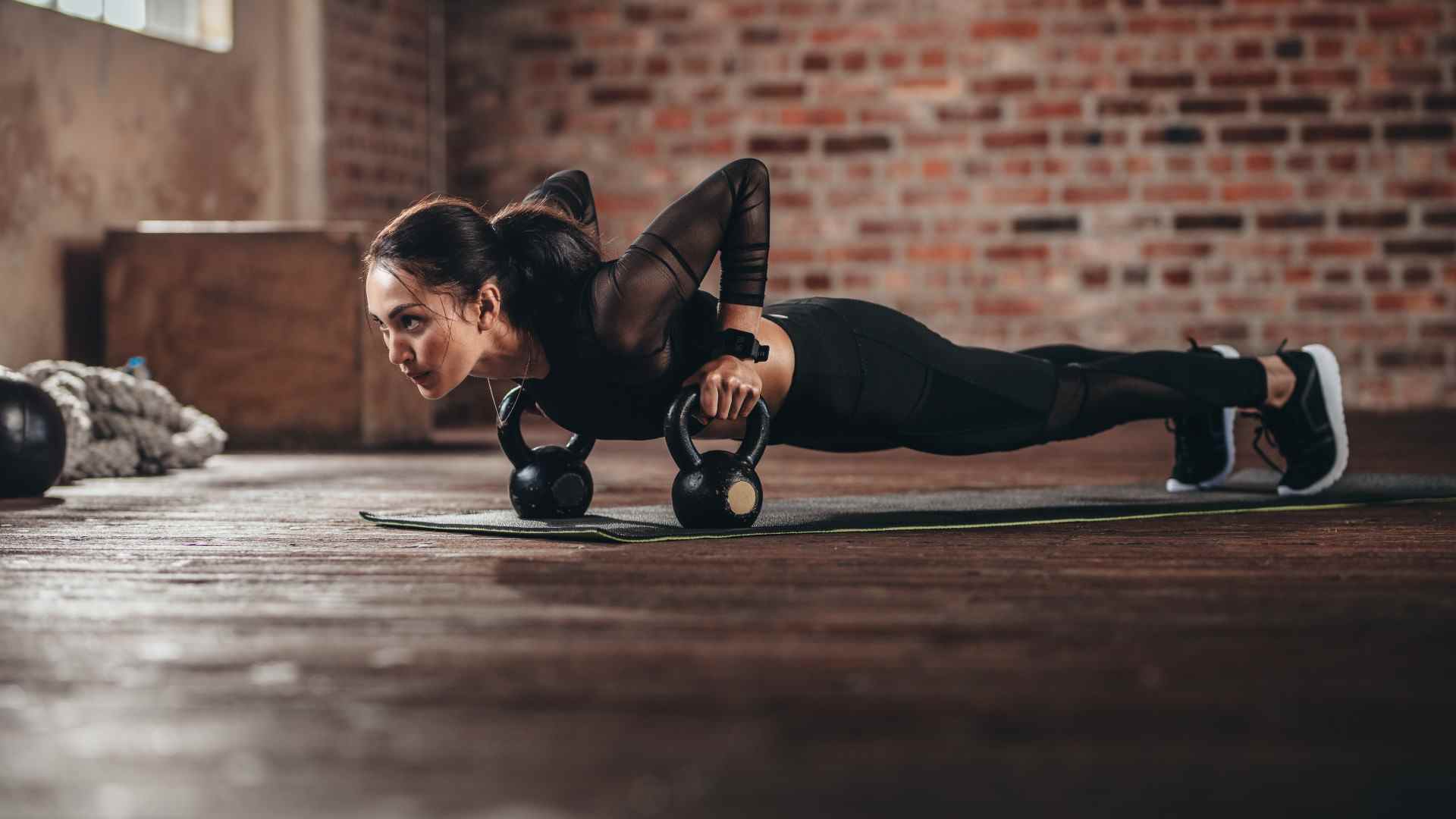 Femme exécutant un push-up déficitaire négatif tenant deux kettlebells dans ses mains dans une salle de sport