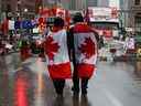 Des personnes ornées de drapeaux canadiens se promènent au milieu de la manifestation des camionneurs du Freedom Convoy contre les mandats de vaccination et d'autres mesures COVID à Ottawa le 17 février 2022. 