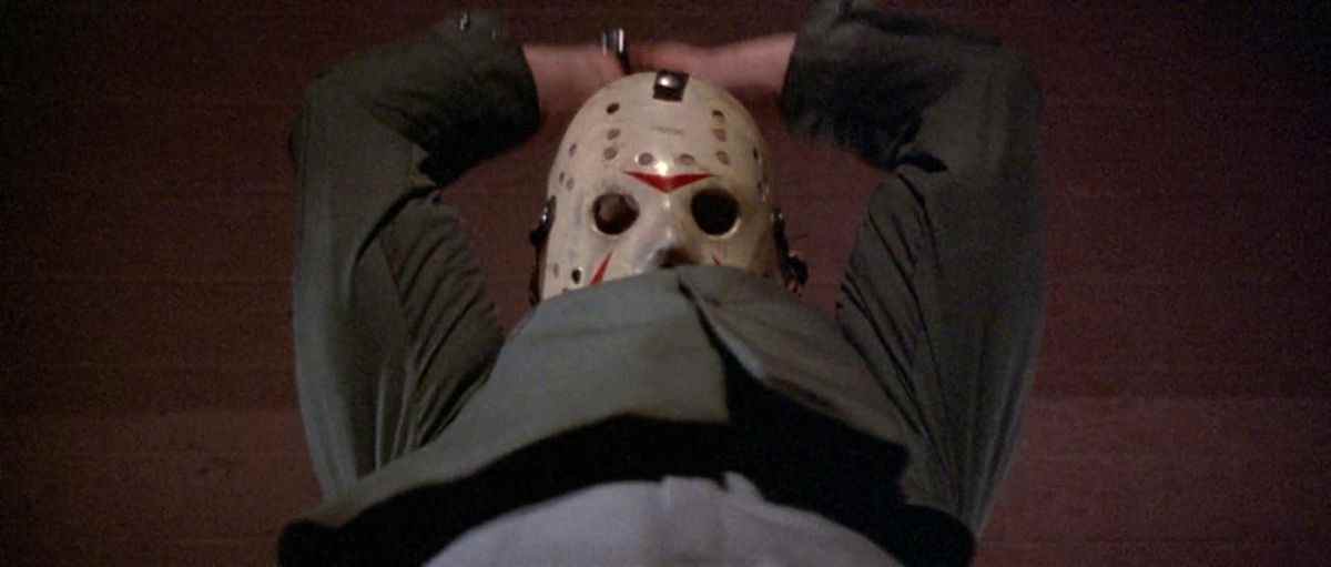 Jason Voorhees, portant son masque de hockey signature, tient les deux mains au-dessus de sa tête sur le point de trancher quelqu'un dans Vendredi 13, partie III.