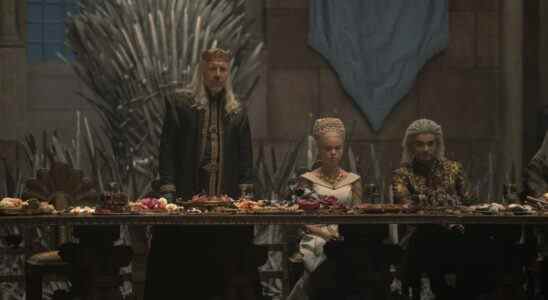 Three people at a long table in front of an iron throne; a man with long blonde hair, wearing a crown; his daughter in a white wedding dress with an elaborate blonde updo; the groom wearing gold and black; still from "House of the Dragon."