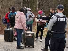 Les demandeurs d'asile parlent à un policier lorsqu'ils traversent le Canada depuis la frontière américaine près d'un point de contrôle sur le chemin Roxham près de Hemmingford, Québec, Canada le 24 avril 2022. Photo prise le 24 avril 2022. REUTERS/Christinne Muschi