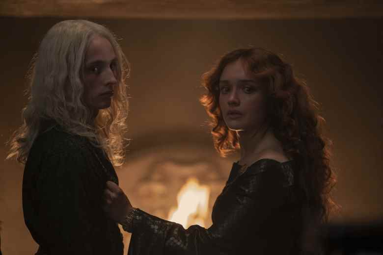 Un adolescent aux longs cheveux blonds et sa mère aux longs cheveux auburn, vêtus d'une tenue de nuit médiévale et debout devant une cheminée;  encore de 