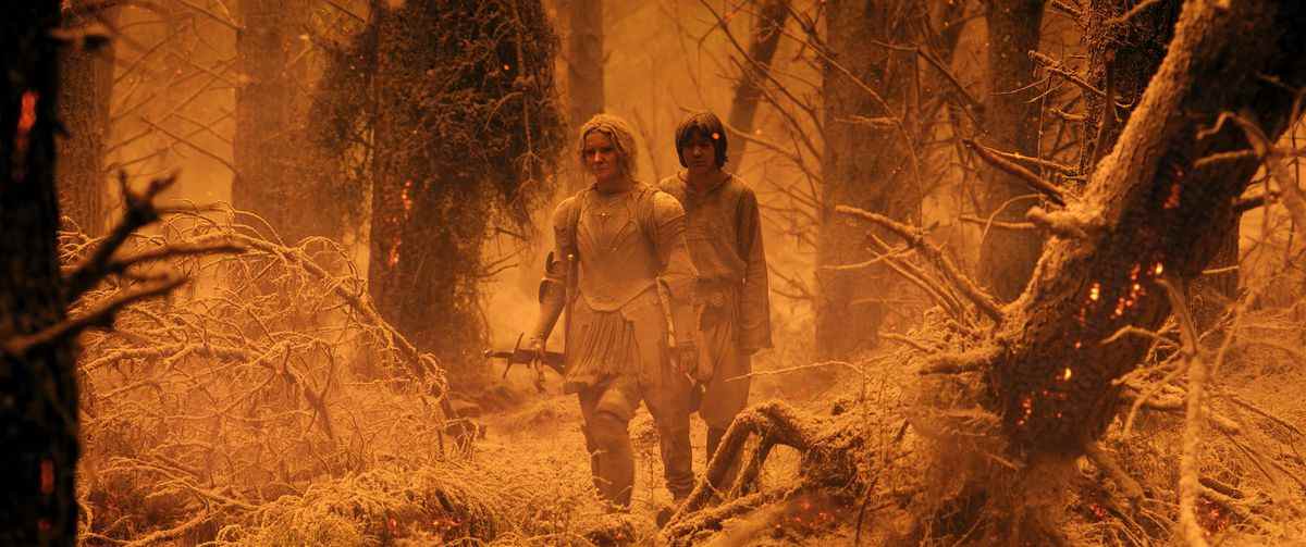 Galadriel et Theo marchant dans un Southlands post-éruption.  Ils sont à mi-distance, et tout est filtré orange et il y a de la cendre partout