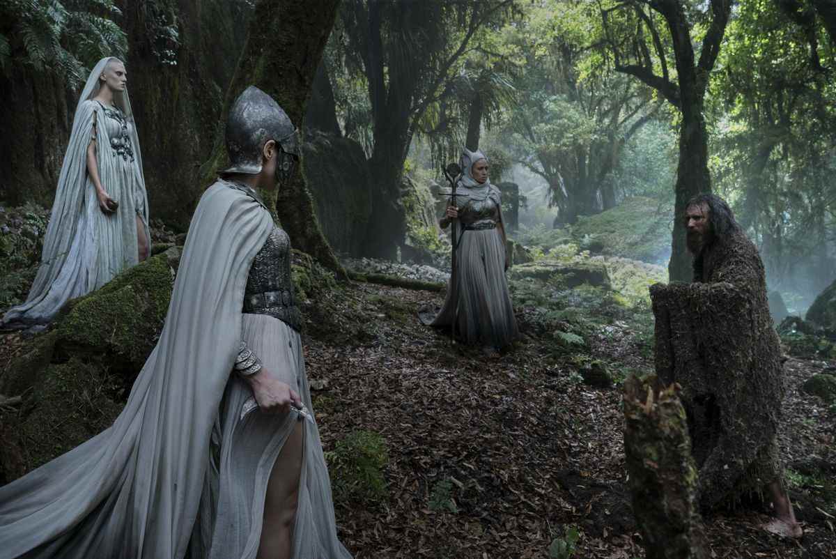 L'Étranger affronte trois guerriers à cape blanche se tenant en triangle dans la forêt dans Rings of Power