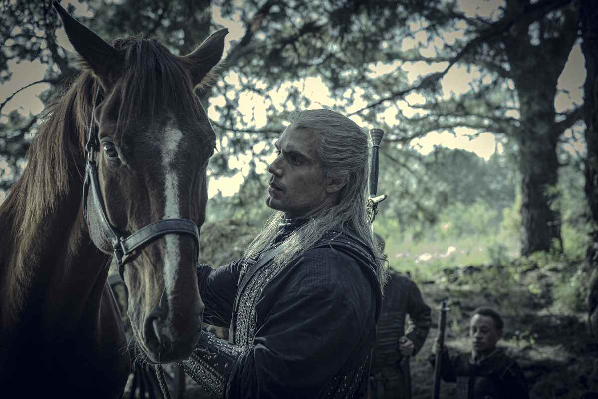 Henry Cavill dans le rôle de Geralt caresse son cheval Roach dans une zone forestière verdoyante