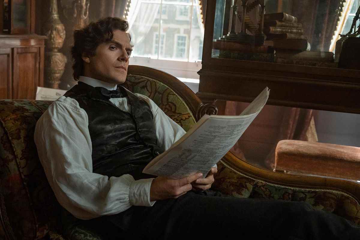 Henry Cavill dans le rôle de Sherlock Holmes.  il est assis sur une chaise longue, scrutant quelques papiers dans ses mains