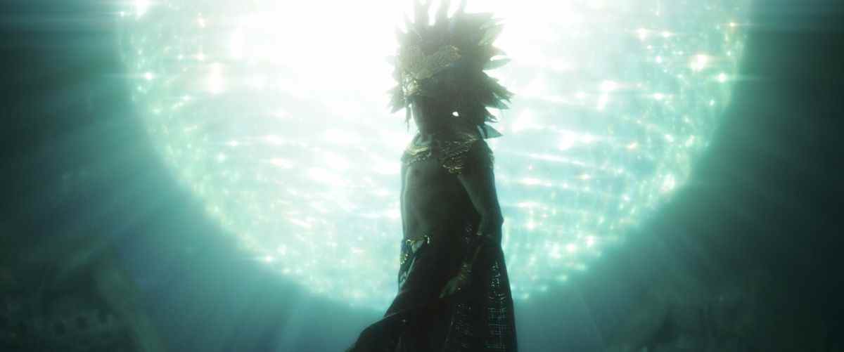 Un homme portant une coiffe de plumes élaborée (joué par Tenoch Huerta) et une cape nage devant une gigantesque sphère lumineuse dans Black Panther: Wakanda Forever.