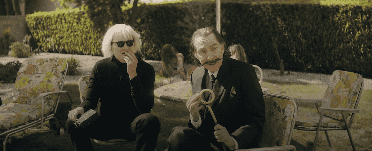 Conan O'Brien dans le rôle d'Andy Warhol et Emo Philips dans le rôle de Salvador Dalí sont assis dans des chaises de jardin à motifs de fleurs et regardent hors champ dans Weird: The Al Yankovic Story
