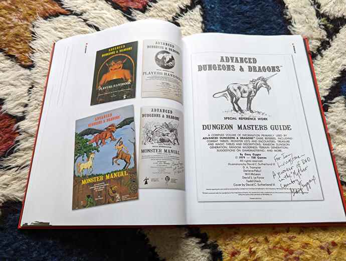 Une photo du livre Dice Men Games Workshop, montrant deux pages d'accessoires originaux de Dungeons & Dragons, y compris une copie de Advanced D&D signée par le co-créateur Gary Gygax.