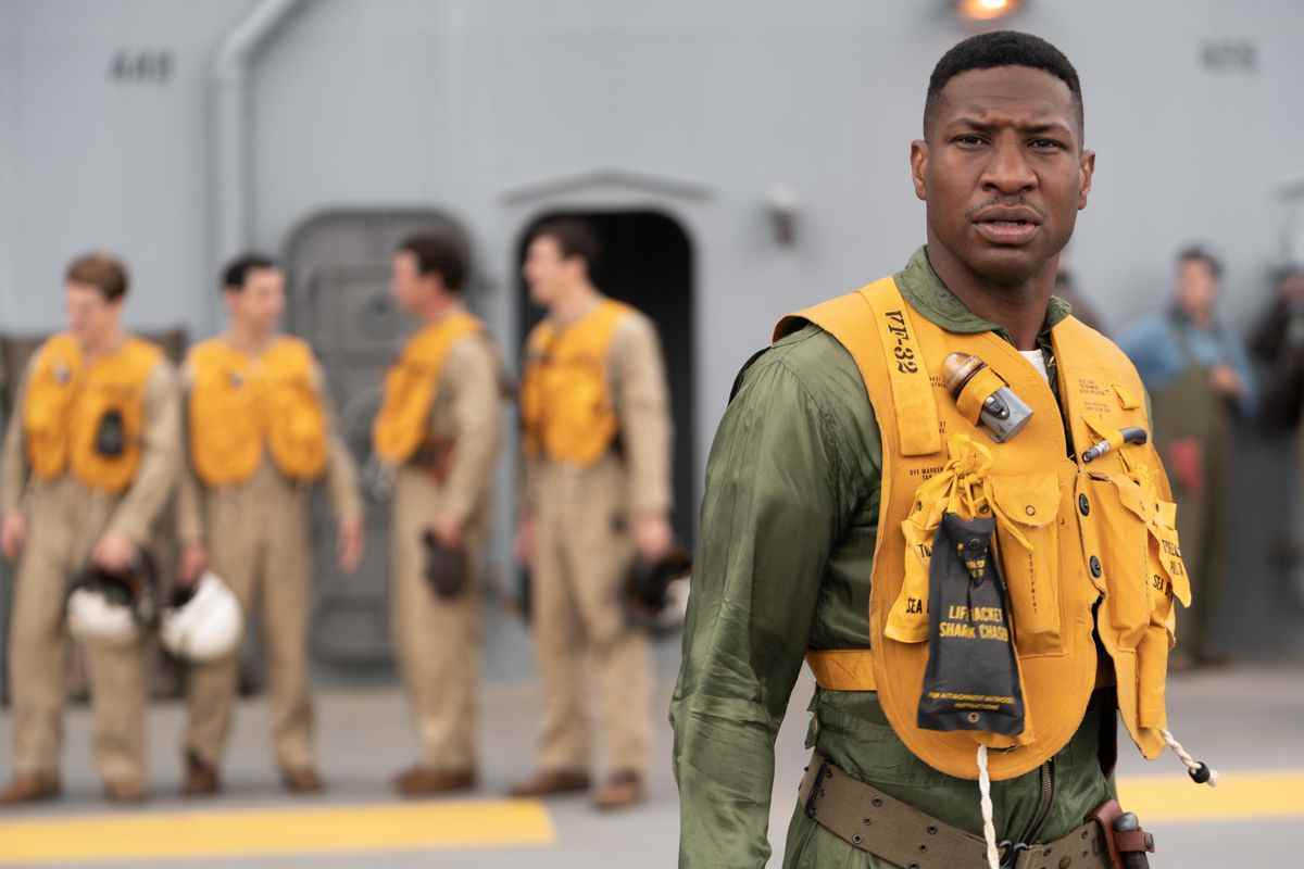 Jesse Brown (Jonathan Majors) se tient sur le pont d'un navire en tenue de pilote de chasse de la Marine et un gilet de sauvetage gonflable dans Devotion