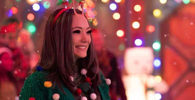 A female-presenting alien with mid-length dark hair, large eyes, and two insect-like antennae, smiling as she wears a green holiday sweater while surrounded by twinkling lights; still from "The Guardians of the Galaxy Holiday Special."