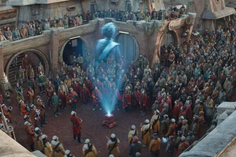 Hologramme bleu-blanc du torse d'une femme projeté à partir d'un petit robot pour une foule massive sur une place publique ;  encore de "Andor."