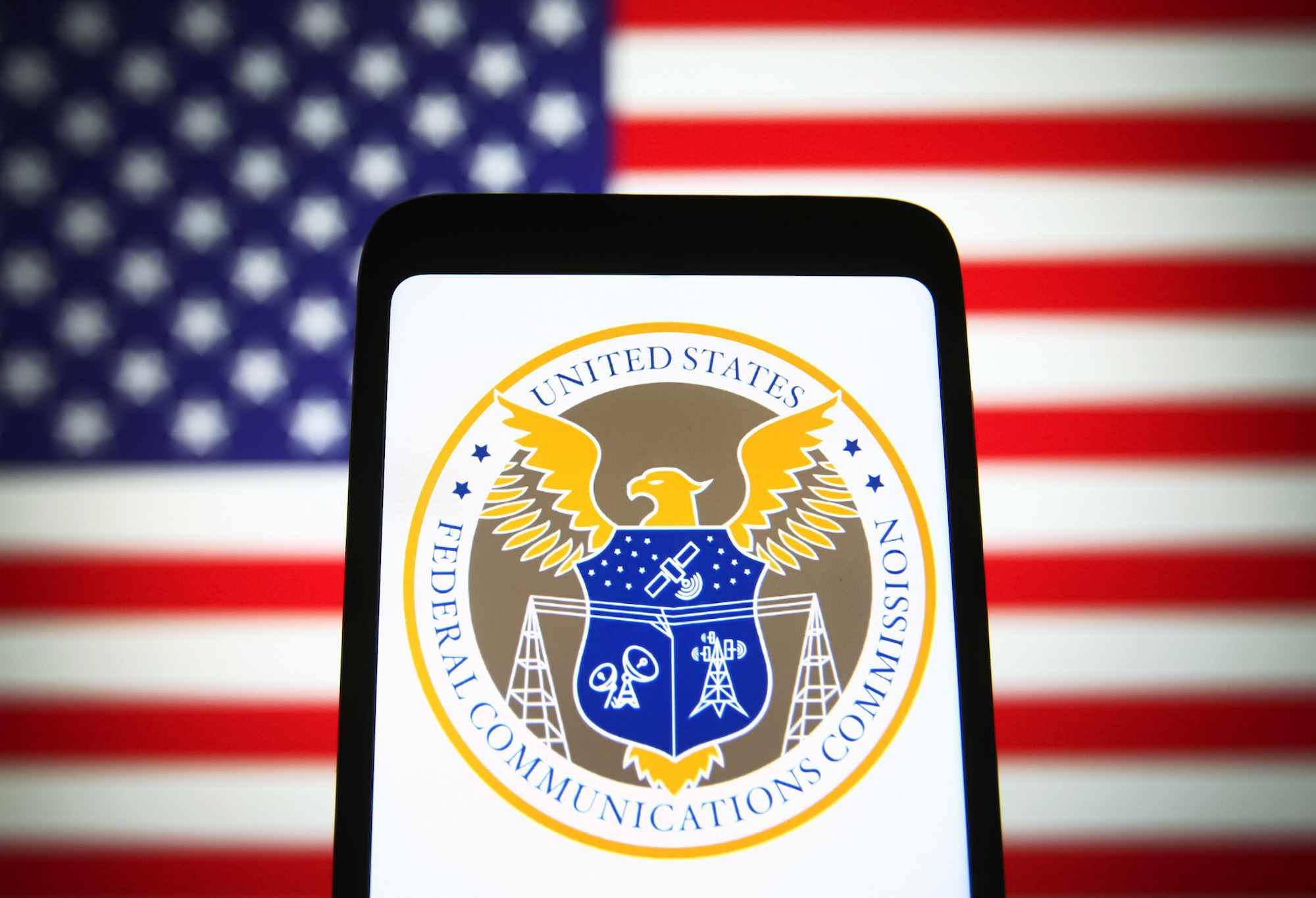 Le sceau de la Federal Communications Commission (FCC) des États-Unis est visible sur l'écran d'un smartphone avec le drapeau américain en arrière-plan.