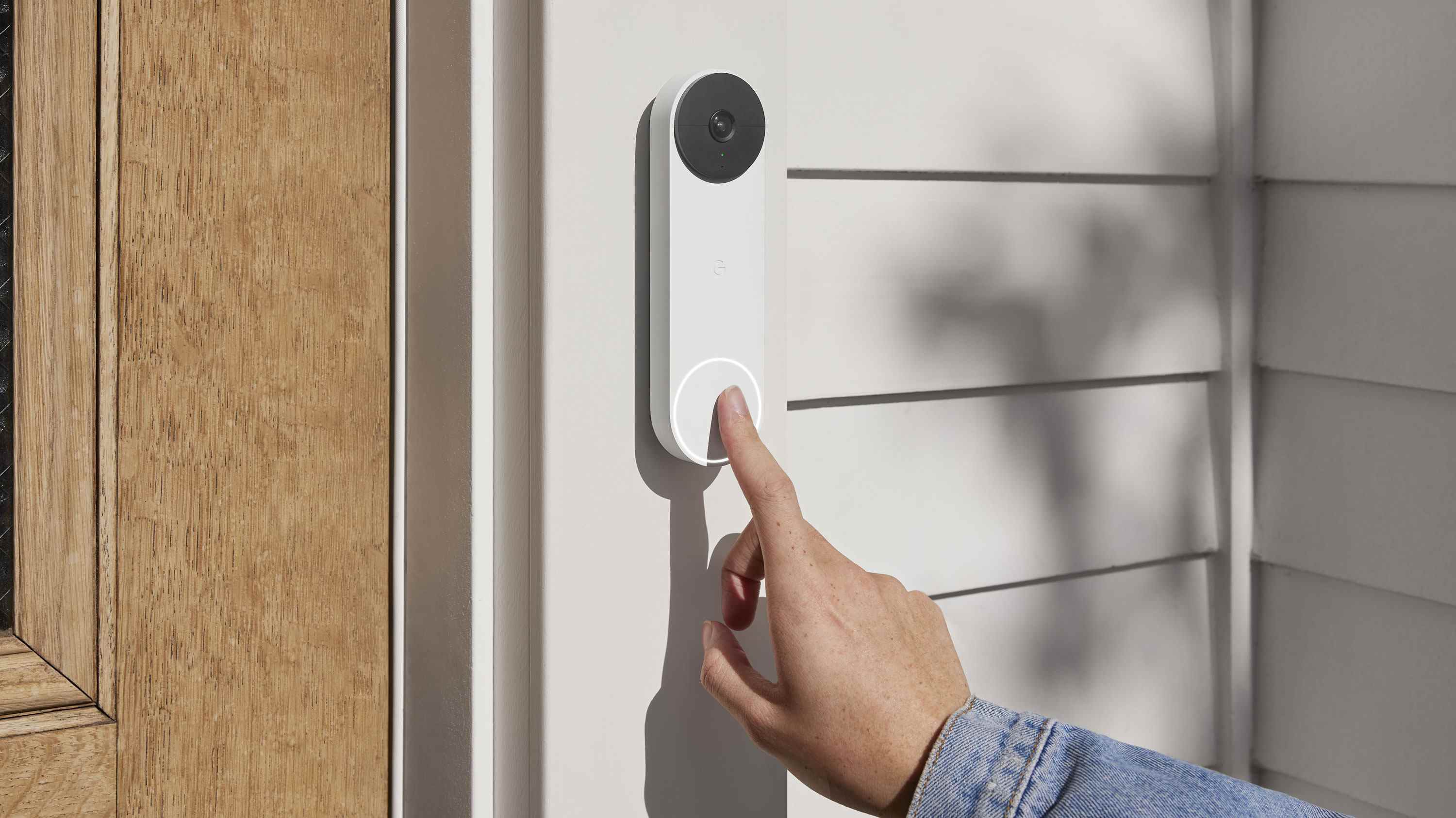 Une main appuie sur le bouton de la Nest Doorbell montée sur un cadre de porte