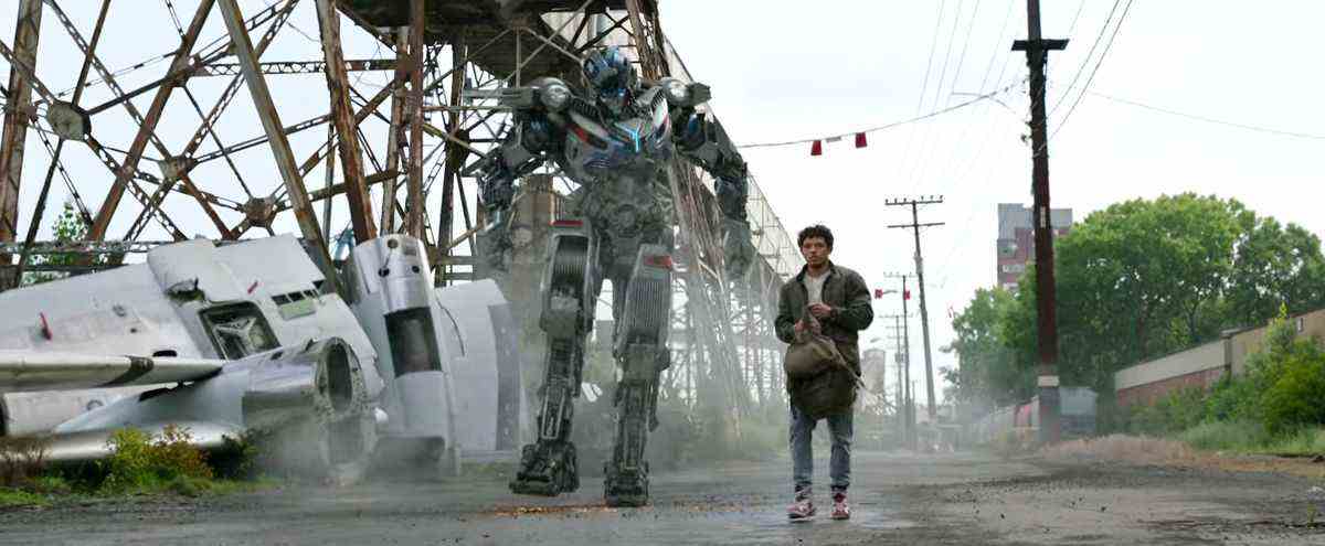 Mirage et un homme hispanique portant un sac à dos marchent le long d'une route poussiéreuse dans Transformers: Rise of the Beasts