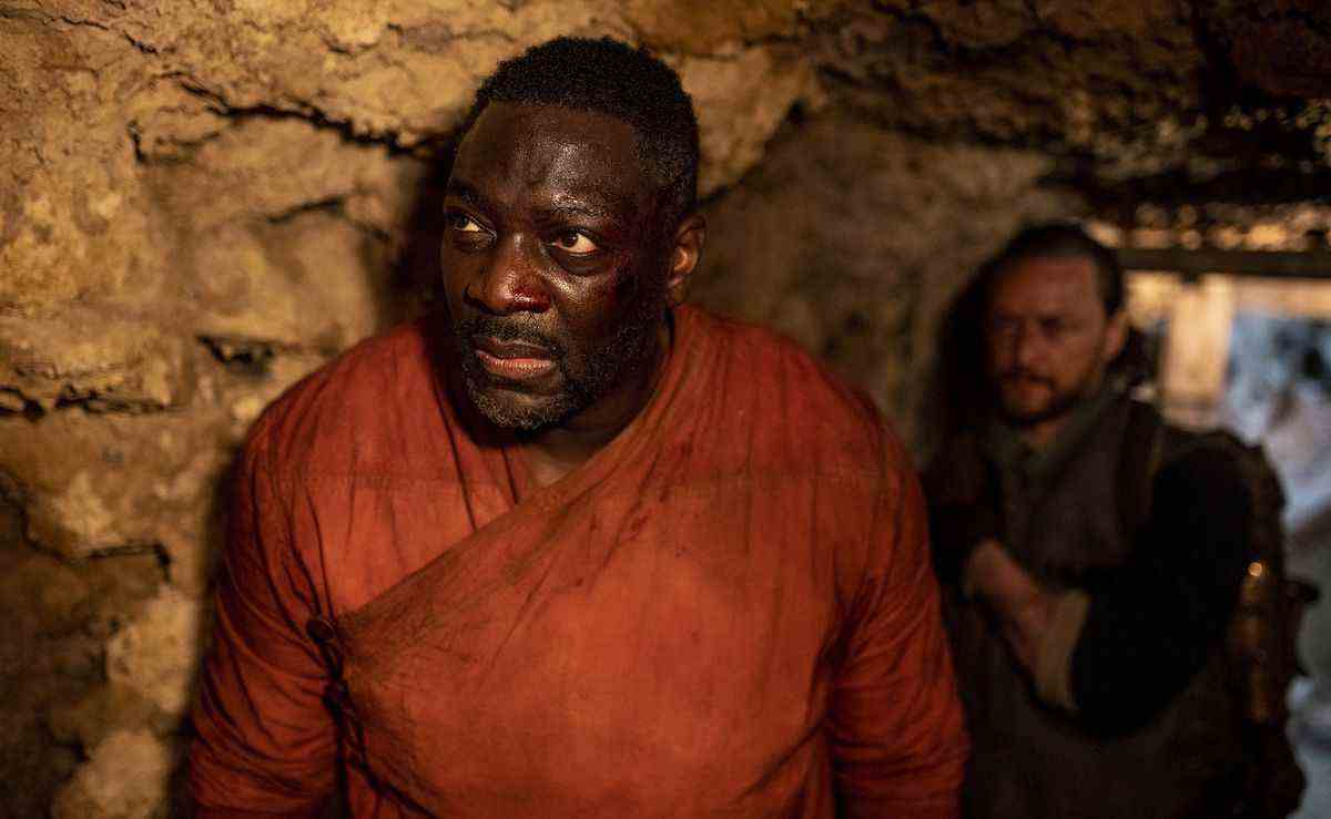 Le commandant Ogunwe (Adewale Akinnuoye-Agbaje) debout dans une grotte regardant quelque chose avec Asriel (James McAvoy) derrière lui dans une photo de la saison 3 de His Dark Materials