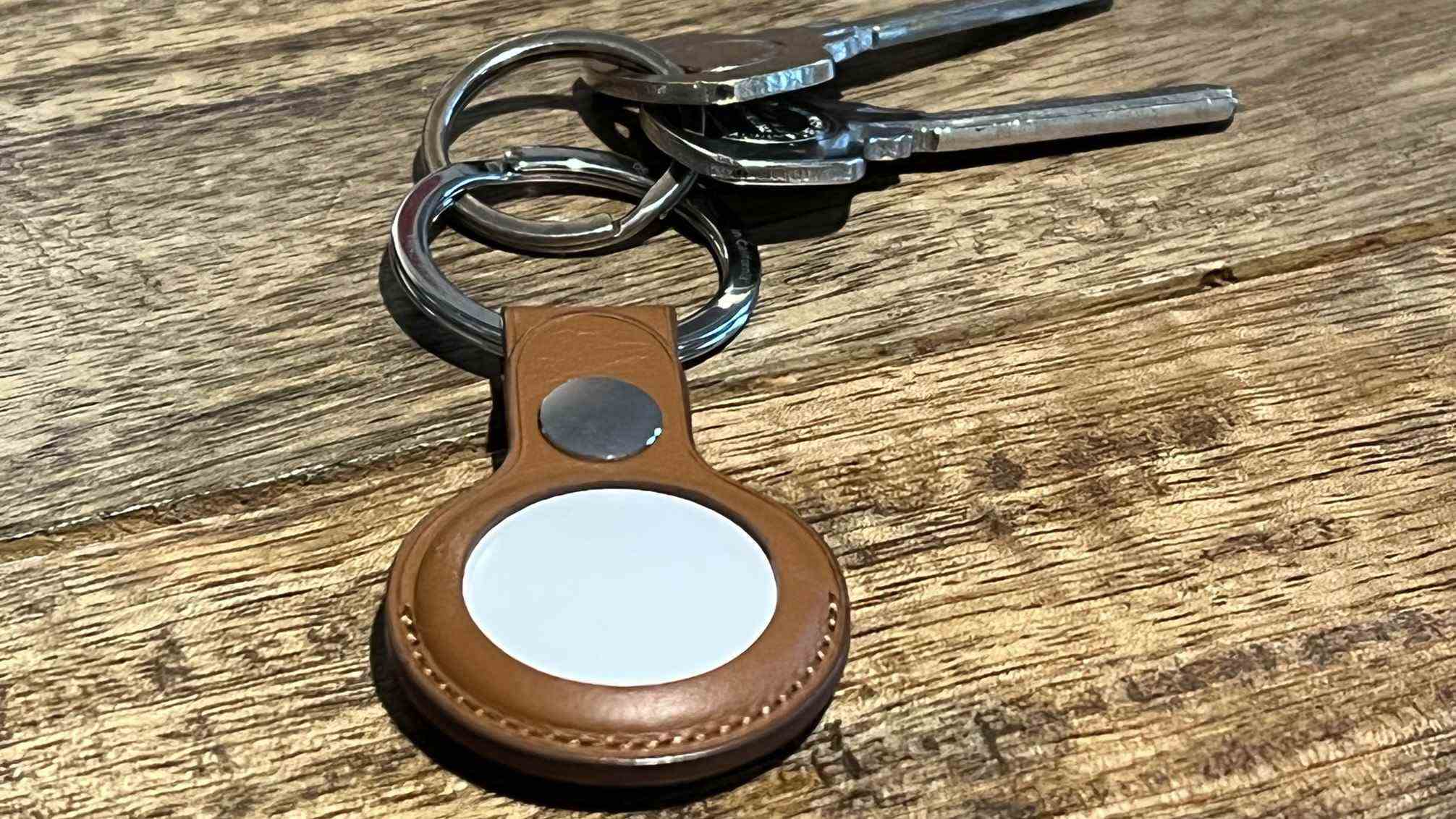 un Apple AirTag dans un porte-clés en cuir marron, attaché à certaines clés sur une surface en bois