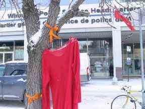 Une robe rouge – symbole des femmes, des filles et des personnes bispirituelles autochtones qui ont été victimes de violence – est accrochée à l'extérieur du quartier général de la police de Winnipeg le mardi 6 décembre 2022, où la police de Winnipeg a tenu une conférence de presse pour répondre aux questions concernant la recherche de reste dans une décharge au nord de la ville.  On pense que les restes de deux femmes assassinées se trouvent à la décharge de Prairie Green, bien que la police ait déclaré que plusieurs facteurs les empêchaient de chercher là-bas.