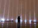 Une femme brave la pluie pour prendre un moment de silence alors que le ciel est éclairé de 14 faisceaux de lumière blanche lors des cérémonies marquant l'anniversaire du massacre à l'École Polytechnique de Montréal, le mardi 6 décembre 2022.