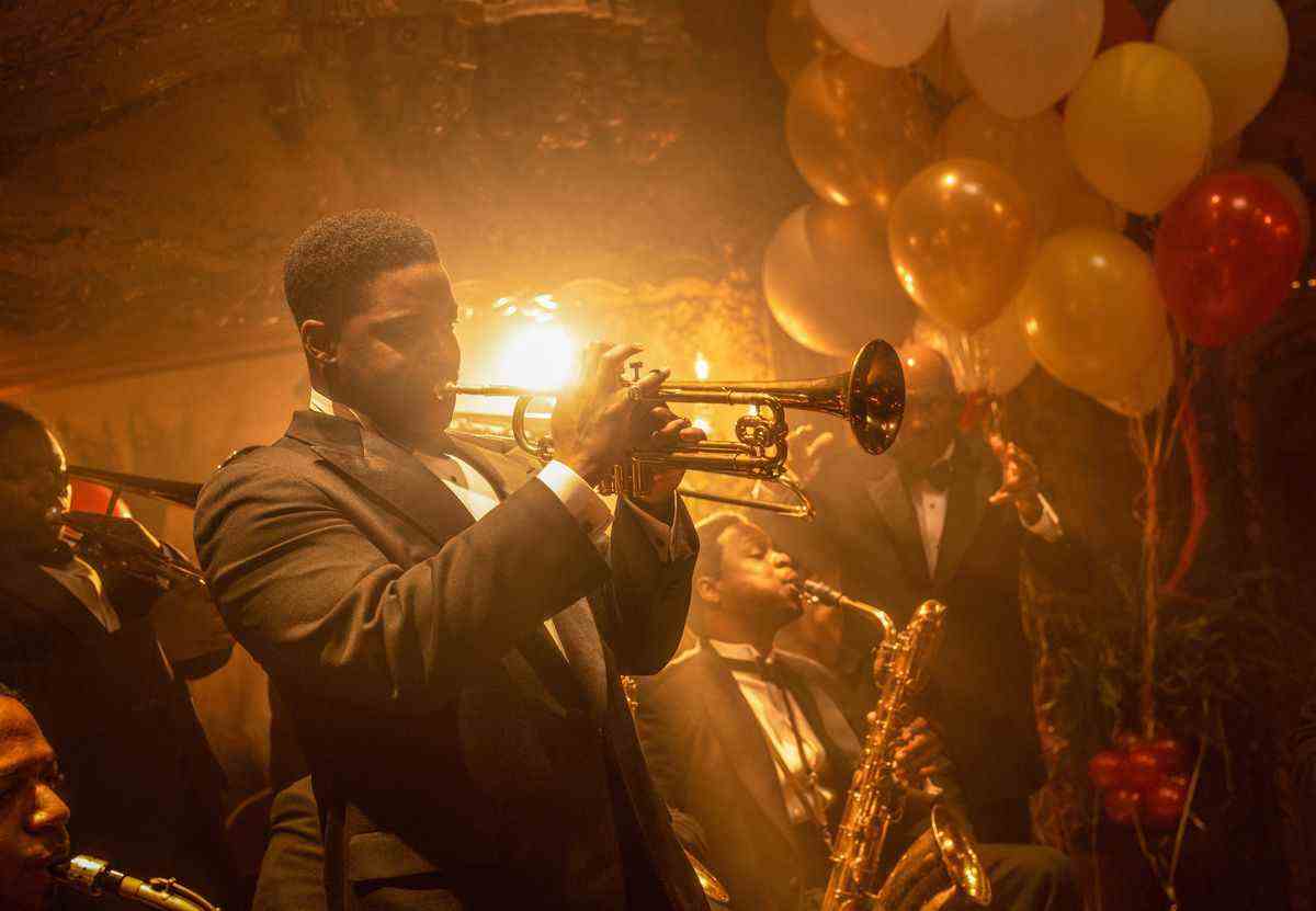 Le trompettiste Sidney Palmer joue du cor avec son groupe, tous vêtus de smokings contre la lueur dorée et les ballons de la fête débauchée autour d'eux dans le film Babylon