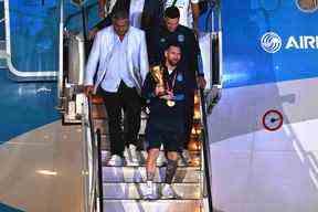 Le capitaine et attaquant argentin Lionel Messi (C) détient le trophée de la coupe du monde de la FIFA alors qu'il descend d'un avion à son arrivée à l'aéroport international d'Ezeiza après avoir remporté le tournoi de la coupe du monde Qatar 2022 à Ezeiza, province de Buenos Aires, Argentine le 20 décembre 2022. ( Photo de Luis ROBAYO / AFP)