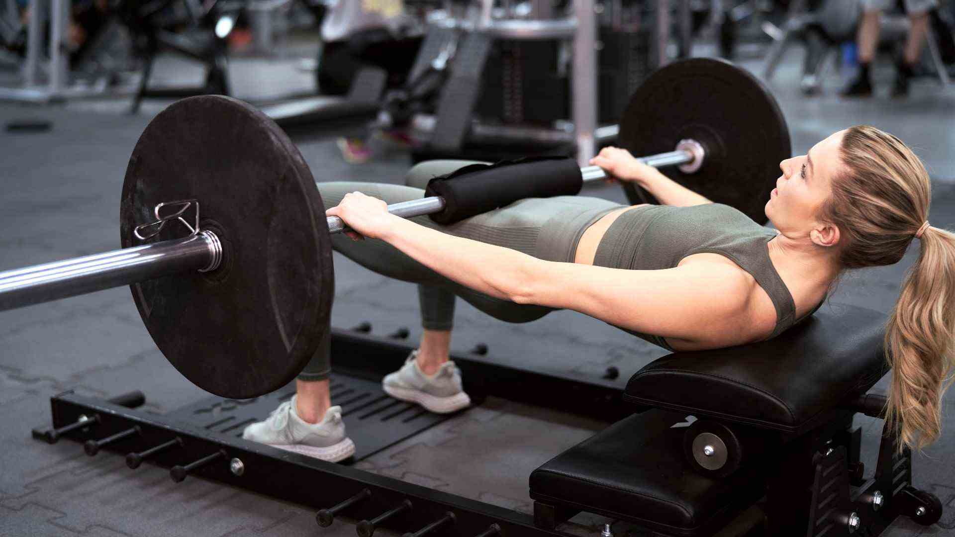 Femme exécutant une poussée de la hanche d'haltères dans la salle de gym sur un banc