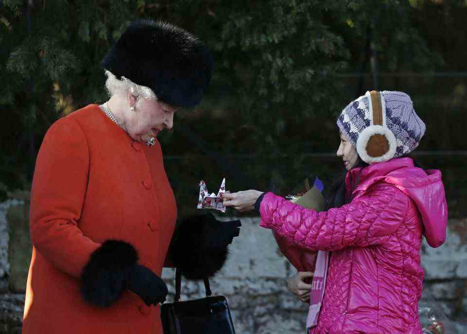 La reine Elizabeth II (à gauche) de Grande-Bretagne reçoit des cadeaux d'enfants après un service religieux traditionnel le jour de Noël à Sandringham, dans l'est de l'Angleterre, le 25 décembre 2013. AFP PHOTO / ADRIAN DENNIS (Photo par Adrian DENNIS / AFP) (Photo par ADRIAN DENNIS/AFP via Getty Images)