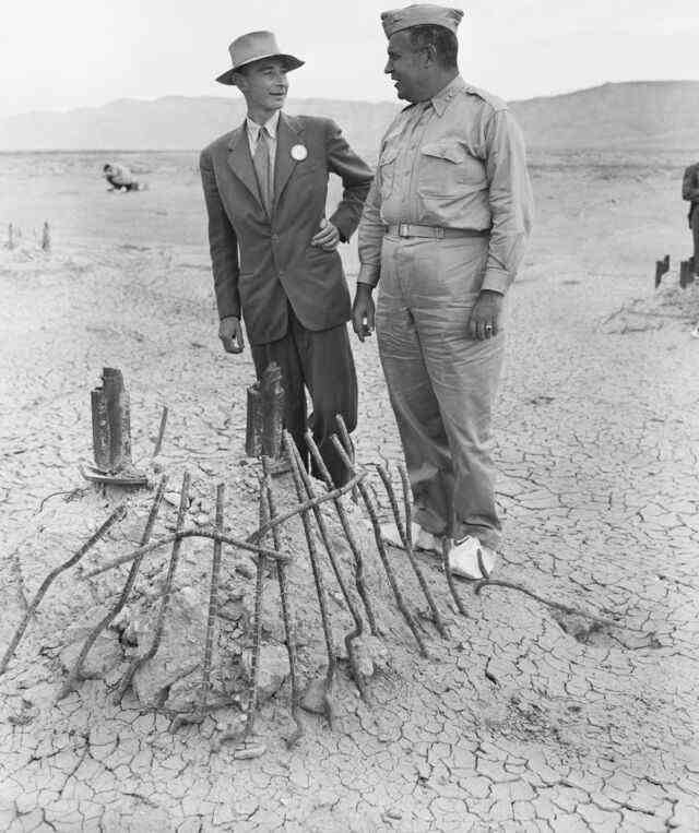 Le major-général Leslie R. Groves (à droite) et J. Robert Oppenheimer voient la base de la tour d'acier sur laquelle la première bombe atomique a été suspendue lors d'un essai près d'Alamogordo, au Nouveau-Mexique, en juillet 1945. La chaleur intense de la bombe a fondu la tour, et a brûlé les sables environnants en cendres vert jade ressemblant à du verre.