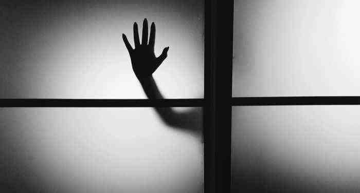 une silhouette d'une main appuyée contre une fenêtre