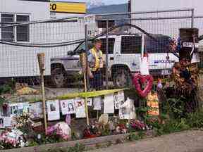 Un agent de la GRC patrouille à l'entrée de la ferme porcine de Port Coquitlam derrière une clôture et un mémorial à certaines des cinquante femmes disparues, alors que la recherche de leurs restes se poursuit à la ferme le mercredi 26 juin 2002.