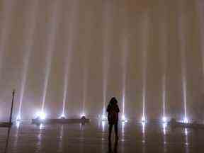 Une femme seule brave la pluie pour prendre un moment de silence alors que le ciel est éclairé de 14 faisceaux de lumière blanche lors des cérémonies marquant l'anniversaire du massacre à l'École Polytechnique de Montréal, le mardi 6 décembre 2022.