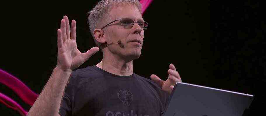 John Carmack speaking in front of a lectern with black and pink background behind