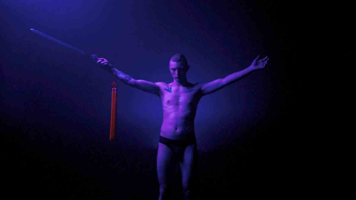 Un homme à Copenhague Cowboy debout dans un néon violet tenant une épée avec ses bras en position Y