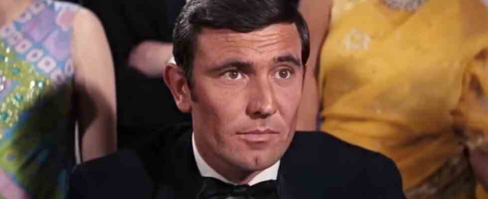 George Lazenby sitting in front of a crowed, dressed in a tuxedo in On Her Majesty