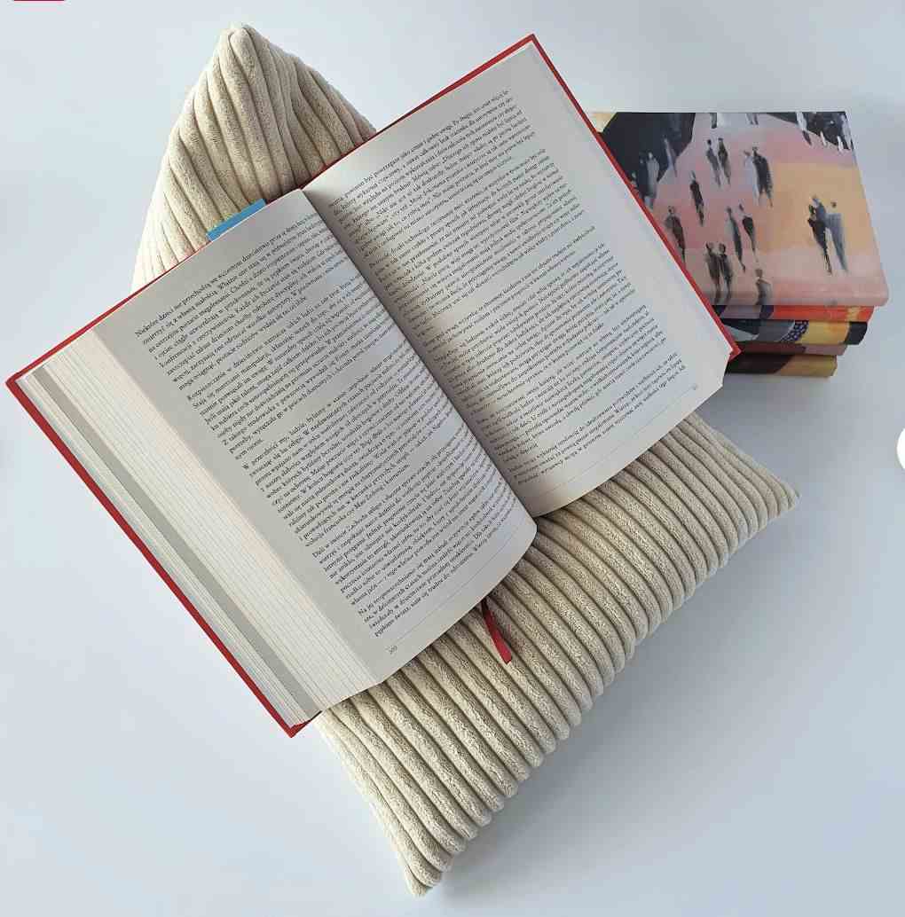 Image d'un coussin de livre en velours côtelé de couleur crème avec un livre ouvert sur le dessus. 