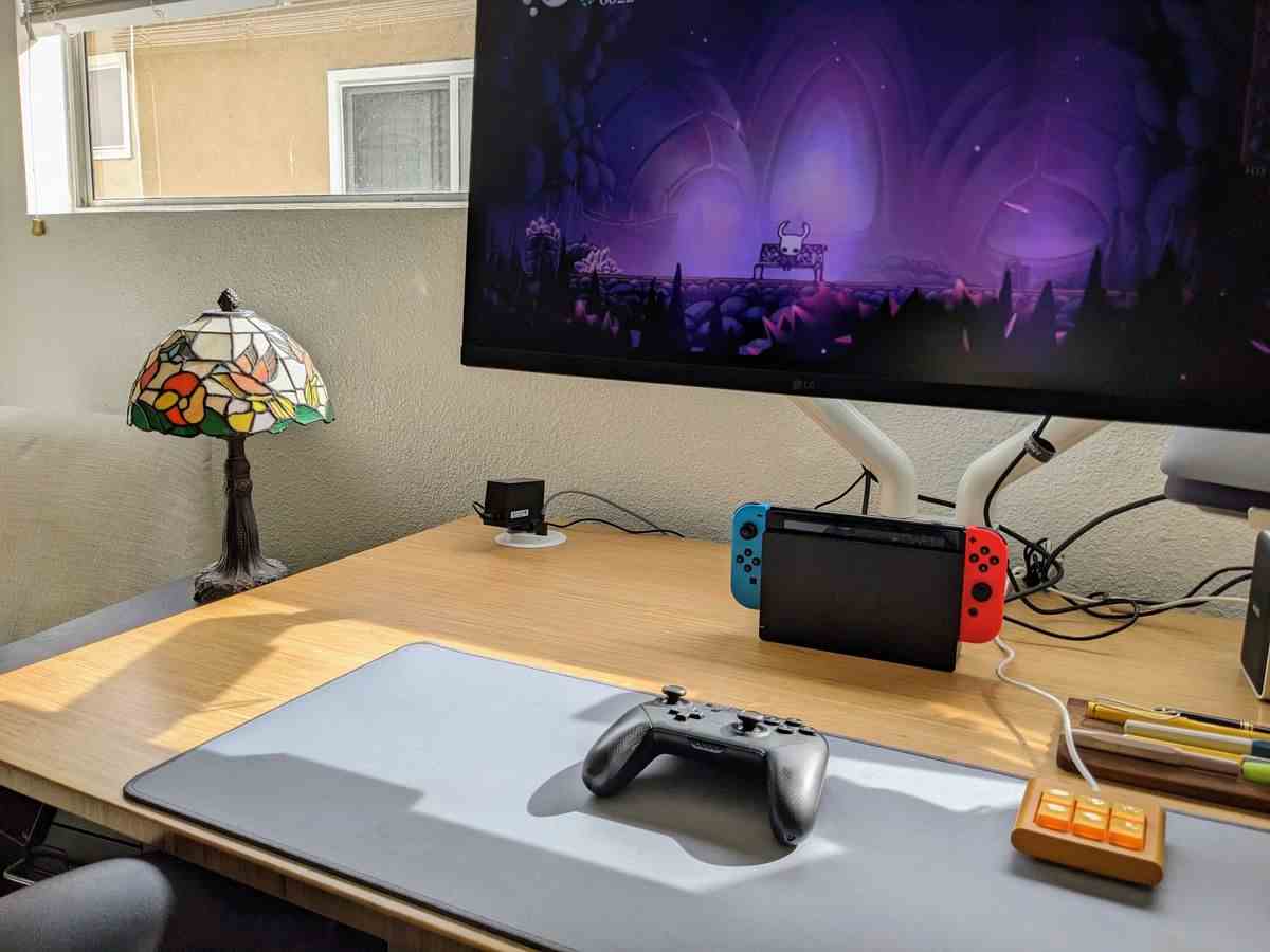 Une configuration de bureau avec une Nintendo Switch et un grand écran de jeu, avec une manette Nintendo Switch pro sur un tapis de bureau.