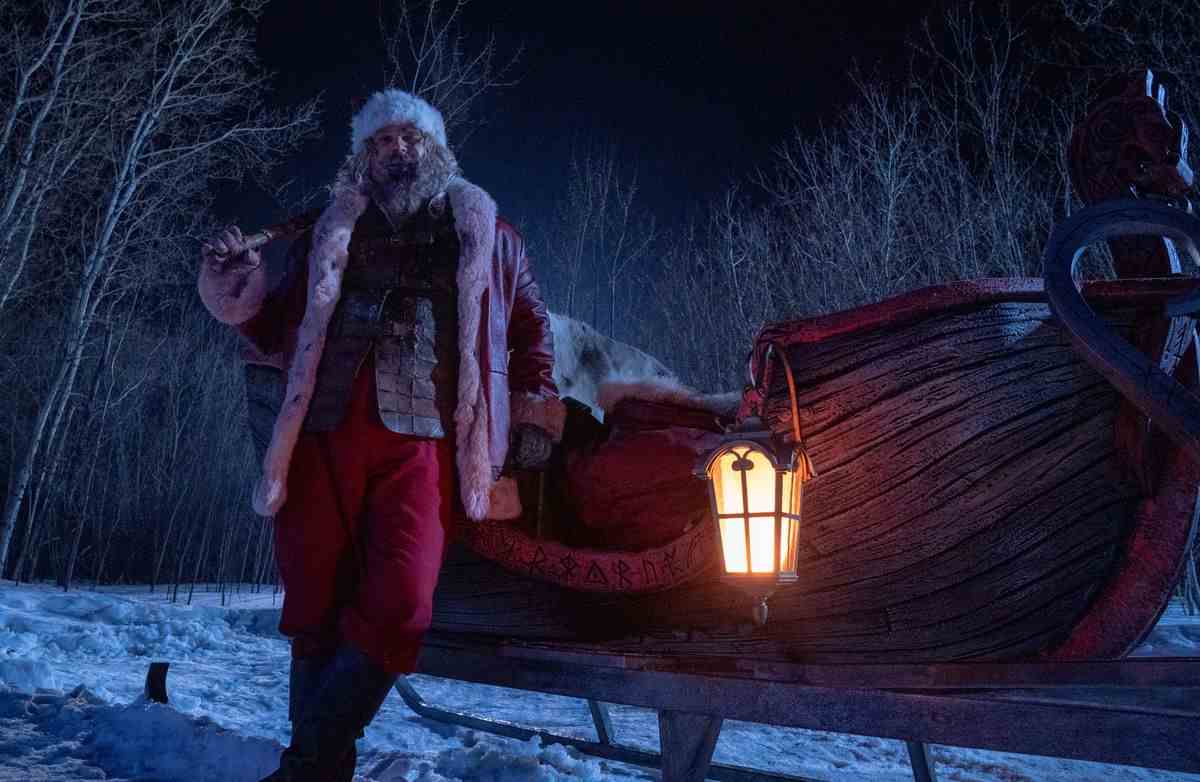 Le Père Noël (David Harbour) s'appuie ivre contre son traîneau, un véhicule en bois rouge sang en forme de bateau sculpté de runes nordiques, dans Violent Night
