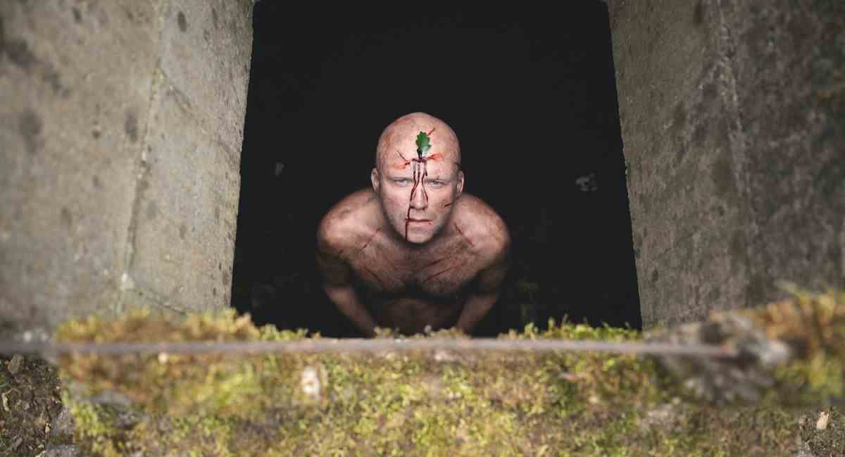 Rory Kinnear lève les yeux d'une fosse, nu, couvert de coupures sanglantes et avec une feuille sur le front dans Men.