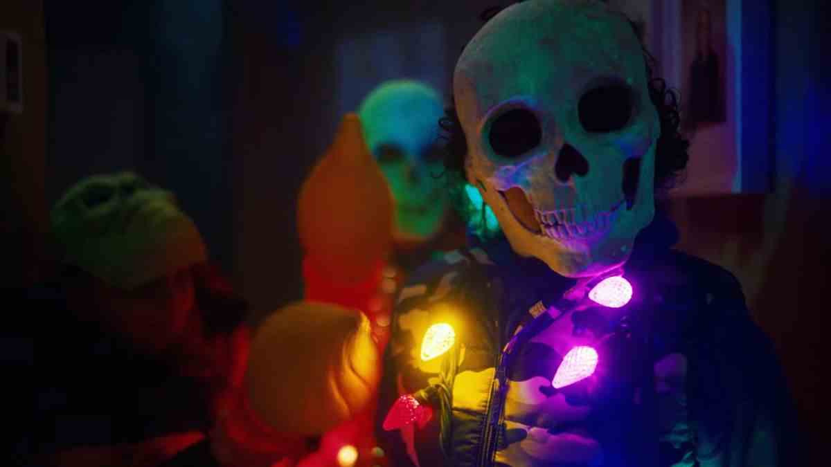 Une personne portant un masque à tête de mort et un costume élaboré avec des lumières multicolores parsemées autour du cou.