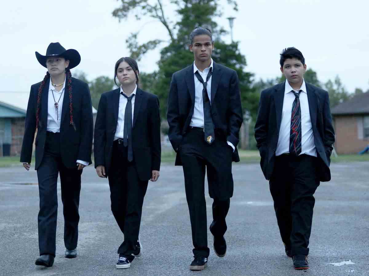 Quatre adolescents en costumes noirs et cravates marchant dans un parking.