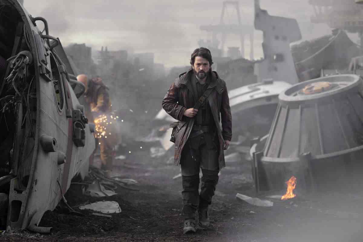 Diego Luna dans le rôle de Cassian Andor traverse un champ de ferraille, avec des machines cassées et en feu.
