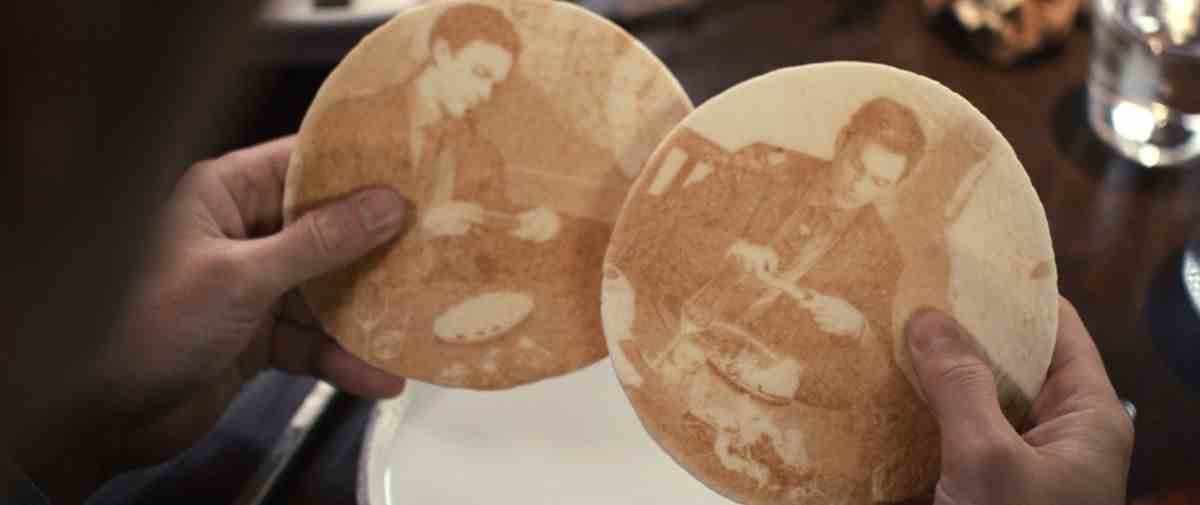 Deux morceaux de pain plat avec des images de Nicholas Hoult prenant des photos de sa nourriture sur iPhone dans The Menu