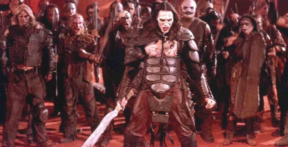 Un guerrier aux cheveux longs à la peau pâle vêtu d'une armure et tenant une épée se tient devant une horde de soldats ressemblant à des zombies.