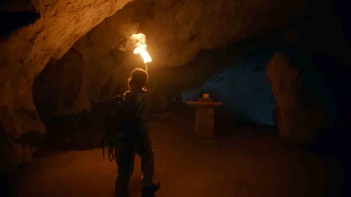 Une femme tenant une torche marche dans une grotte vers un artefact sur un piédestal